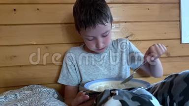 一个非常饥饿的男孩，头发湿漉漉的，坐在农村木屋的床上，贪婪地吃着米饭，他在外面玩耍